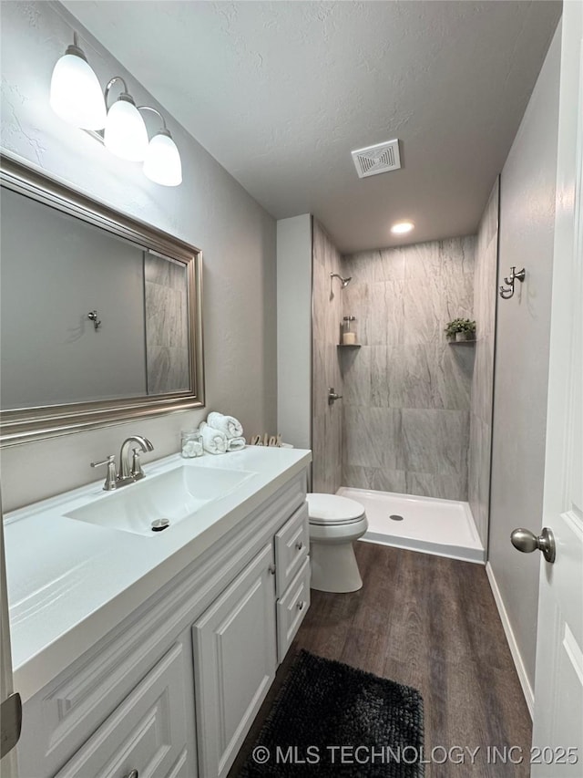 bathroom featuring a tile shower, vanity, wood-type flooring, a textured ceiling, and toilet