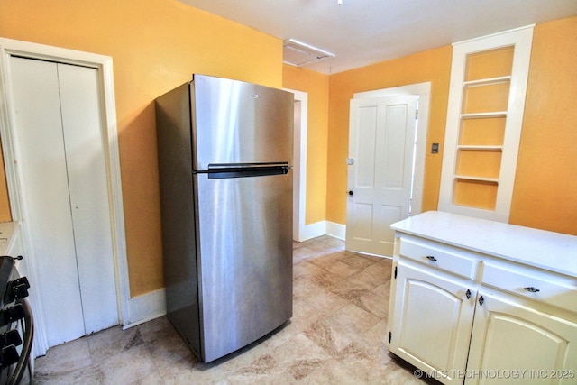 kitchen featuring white cabinetry, stove, and stainless steel refrigerator