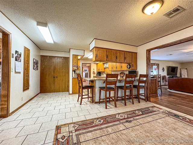 kitchen featuring light tile patterned floors, a kitchen breakfast bar, kitchen peninsula, and a textured ceiling