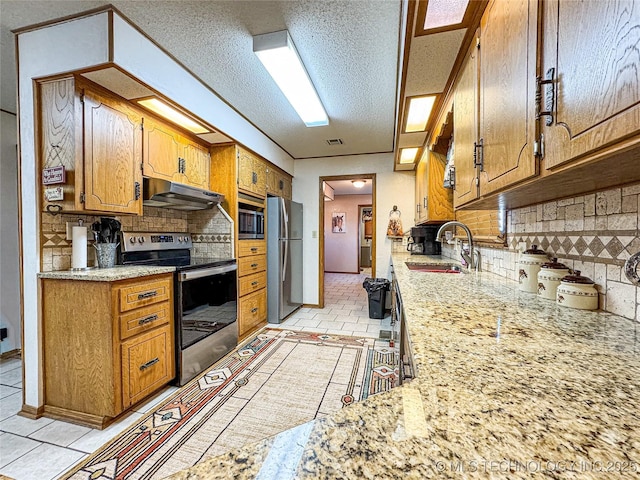 kitchen featuring sink, decorative backsplash, stainless steel appliances, light stone countertops, and a textured ceiling