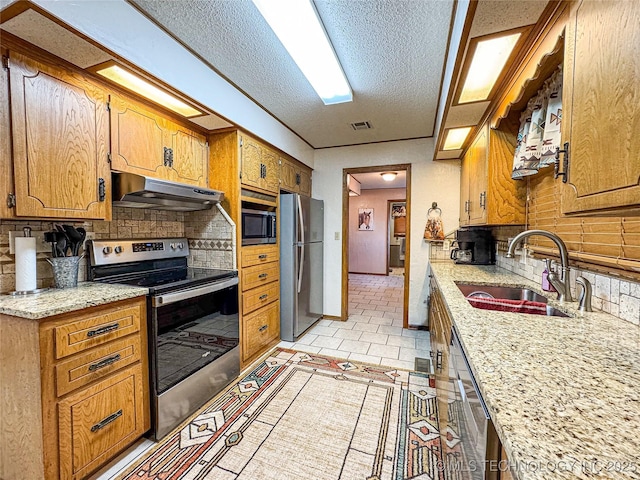 kitchen featuring sink, decorative backsplash, light stone counters, stainless steel appliances, and a textured ceiling