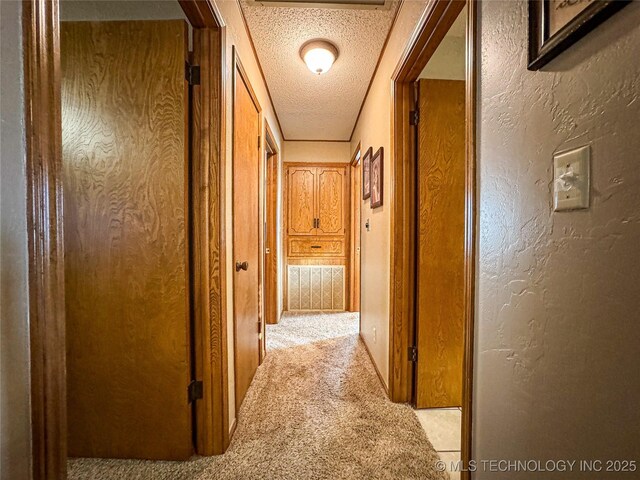 hall with light carpet and a textured ceiling