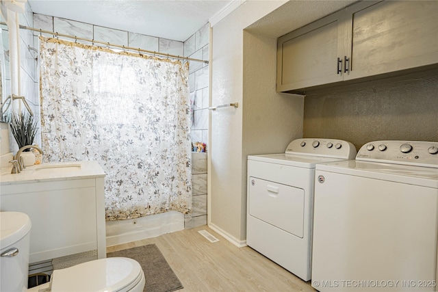 clothes washing area with sink, washing machine and dryer, light hardwood / wood-style floors, and a textured ceiling