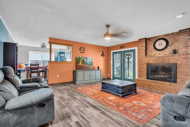 living room featuring french doors, a brick fireplace, a textured ceiling, ceiling fan, and hardwood / wood-style floors