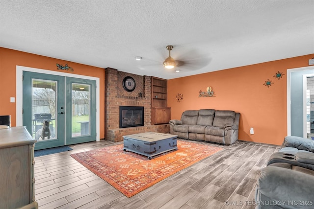 living room featuring french doors, a brick fireplace, a textured ceiling, ceiling fan, and light hardwood / wood-style floors