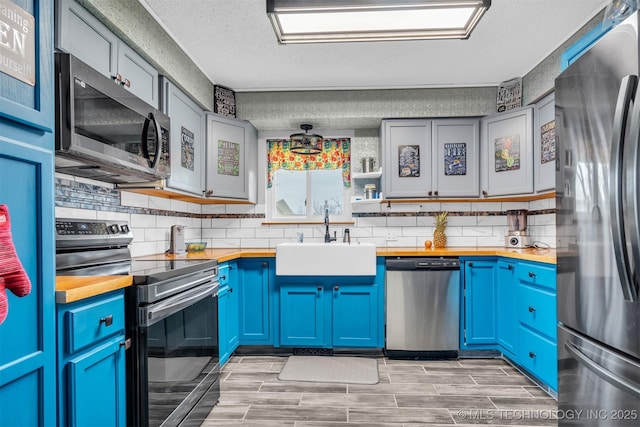 kitchen with appliances with stainless steel finishes, butcher block counters, sink, and blue cabinets