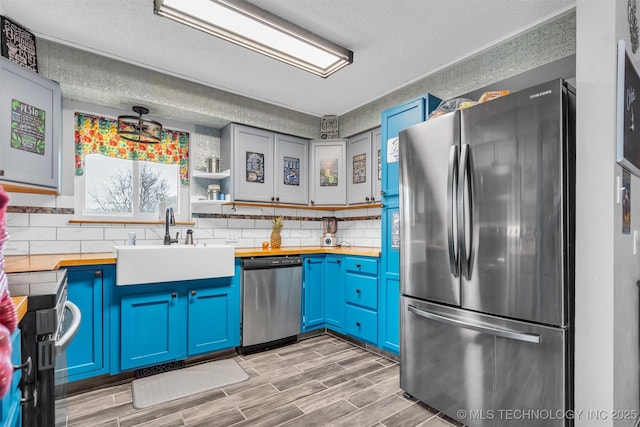 kitchen featuring sink, appliances with stainless steel finishes, butcher block counters, tasteful backsplash, and blue cabinets