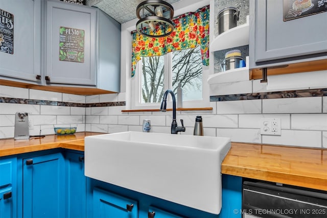 kitchen with tasteful backsplash, butcher block countertops, sink, and blue cabinets