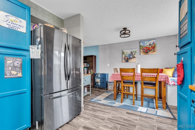 kitchen with stainless steel fridge, a textured ceiling, and blue cabinets