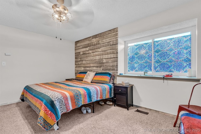 carpeted bedroom with ceiling fan, wooden walls, and a textured ceiling