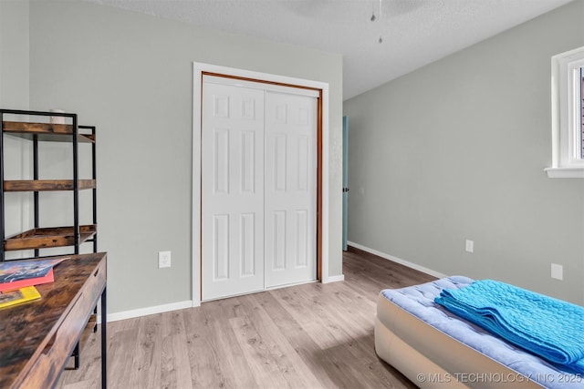 bedroom with a closet, a textured ceiling, and light hardwood / wood-style flooring