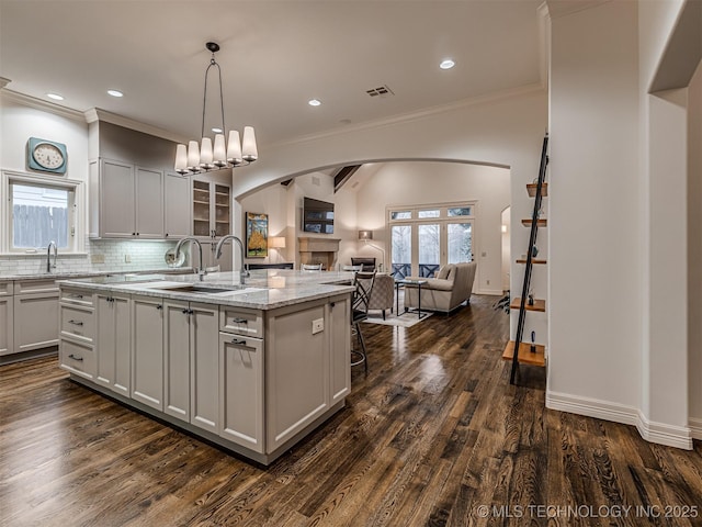 kitchen featuring sink, a center island with sink, dark hardwood / wood-style floors, and light stone counters