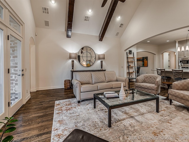 living room featuring ceiling fan with notable chandelier, dark wood-type flooring, high vaulted ceiling, and beam ceiling