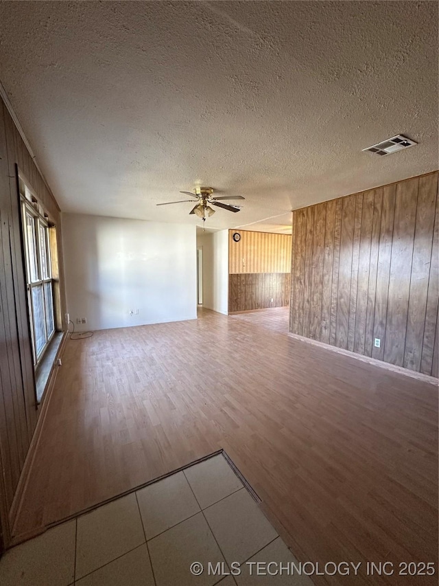 unfurnished living room with hardwood / wood-style flooring, wooden walls, a textured ceiling, and ceiling fan