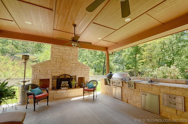 view of patio / terrace with sink, an outdoor stone fireplace, ceiling fan, a grill, and area for grilling