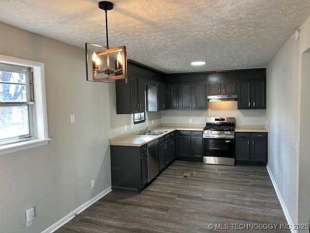 kitchen featuring sink, hanging light fixtures, stainless steel gas range oven, dark wood-type flooring, and a textured ceiling