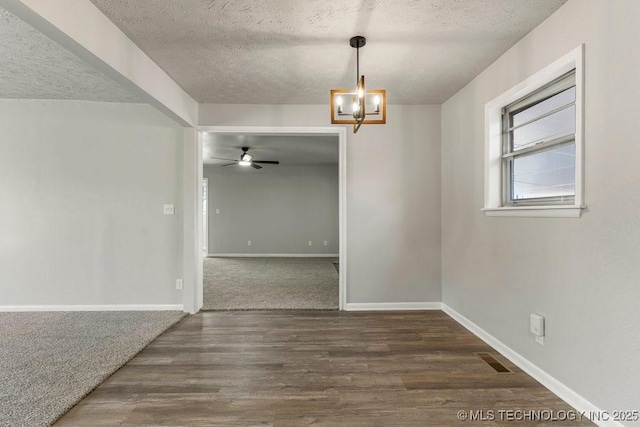 unfurnished dining area with dark hardwood / wood-style flooring, ceiling fan with notable chandelier, and a textured ceiling