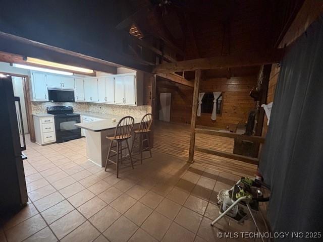 kitchen with a kitchen bar, wood walls, black appliances, kitchen peninsula, and white cabinets