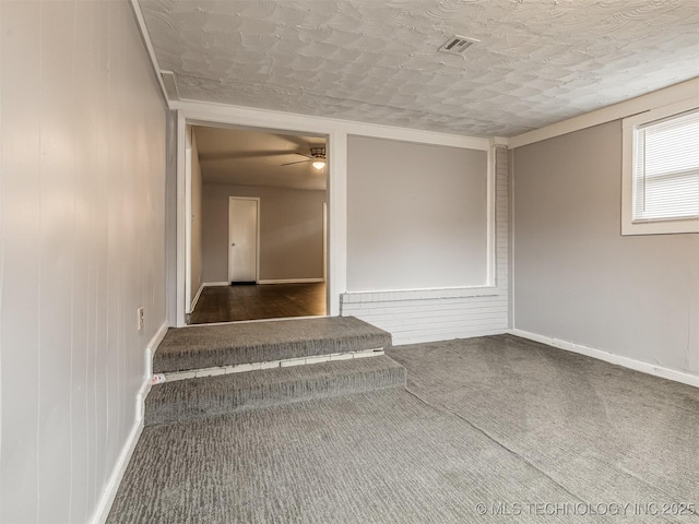 stairs with ceiling fan, wooden walls, carpet, and a textured ceiling