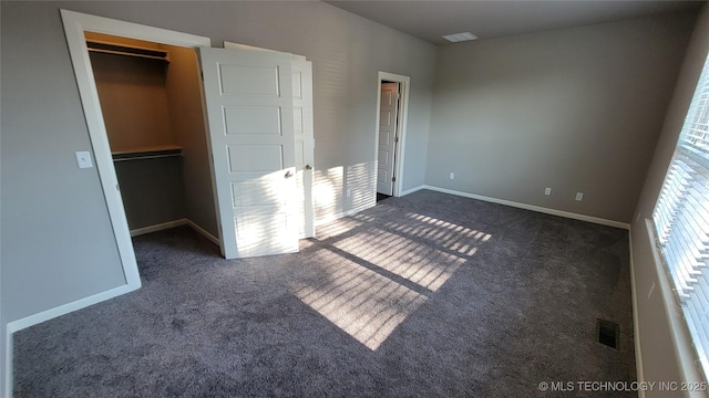 unfurnished bedroom with a walk in closet and dark carpet