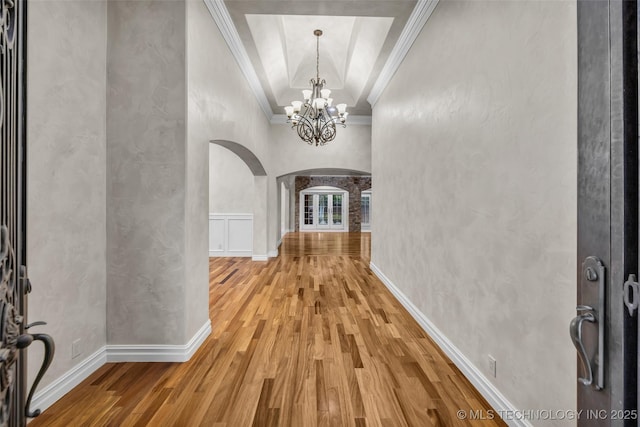 corridor with ornamental molding, a tray ceiling, a chandelier, and hardwood / wood-style floors