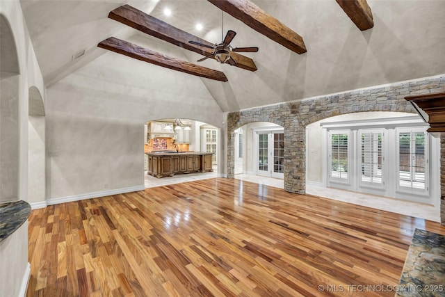 unfurnished living room with ceiling fan with notable chandelier, light hardwood / wood-style flooring, high vaulted ceiling, and beamed ceiling