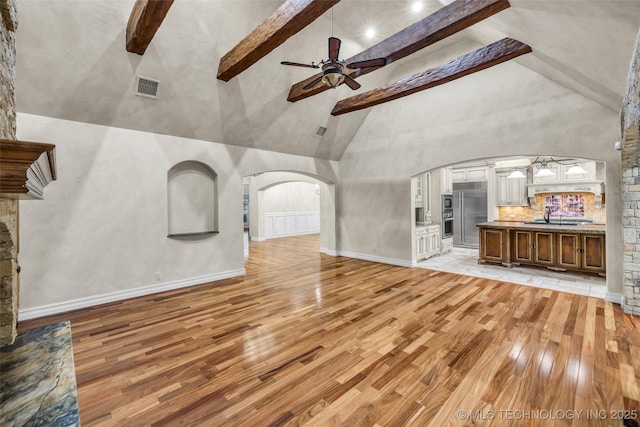 unfurnished living room with sink, high vaulted ceiling, light hardwood / wood-style flooring, beamed ceiling, and ceiling fan