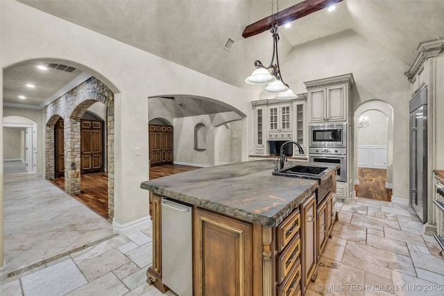 kitchen with pendant lighting, high vaulted ceiling, dark stone countertops, a large island with sink, and stainless steel appliances