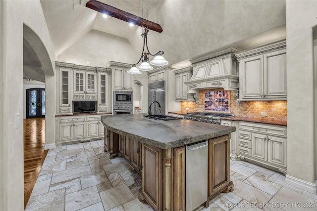 kitchen with pendant lighting, high vaulted ceiling, built in appliances, custom range hood, and a center island with sink