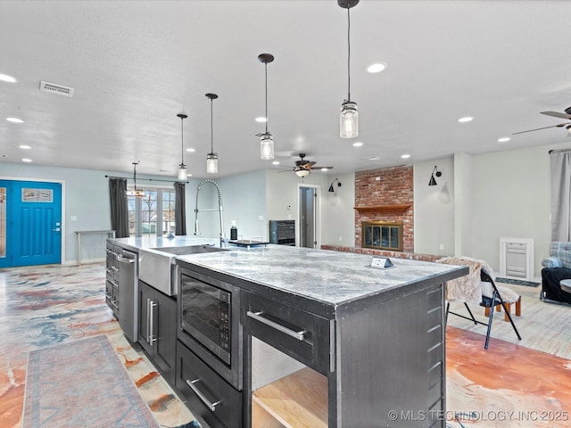 kitchen with pendant lighting, ceiling fan, a kitchen island with sink, and black microwave