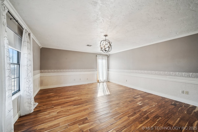 spare room featuring a textured ceiling, dark wood-type flooring, ornamental molding, and a chandelier