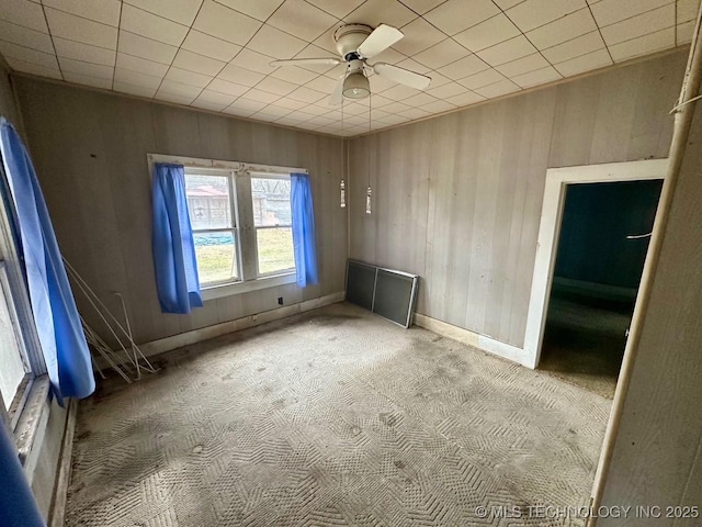 unfurnished room featuring carpet floors, ceiling fan, and wood walls