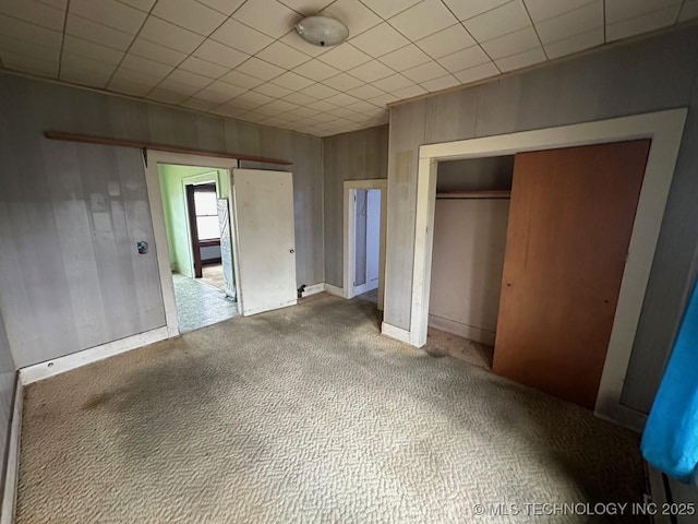 unfurnished bedroom featuring a closet, wooden walls, and carpet