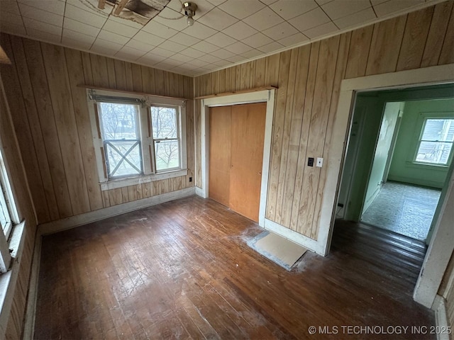 unfurnished bedroom with dark hardwood / wood-style flooring, wooden walls, and a closet