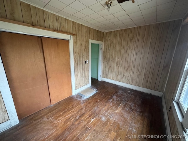 unfurnished bedroom featuring dark hardwood / wood-style flooring, wooden walls, and a closet