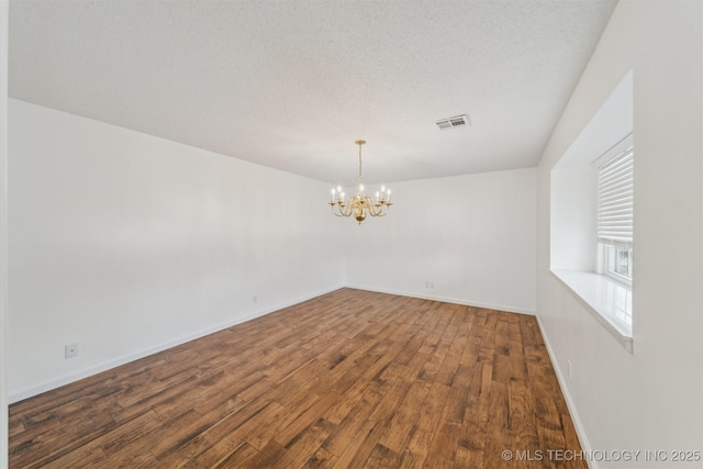 spare room with dark wood-type flooring, a chandelier, and a textured ceiling