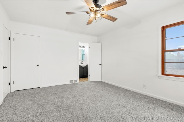 unfurnished bedroom featuring light carpet, sink, ceiling fan, and ensuite bathroom