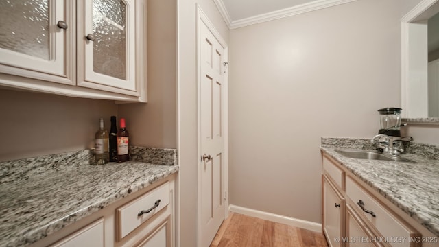 kitchen featuring ornamental molding, sink, light stone counters, and light hardwood / wood-style floors