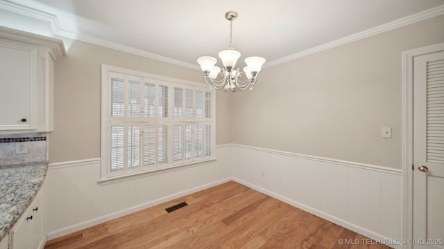 unfurnished dining area with crown molding, a chandelier, and light hardwood / wood-style floors