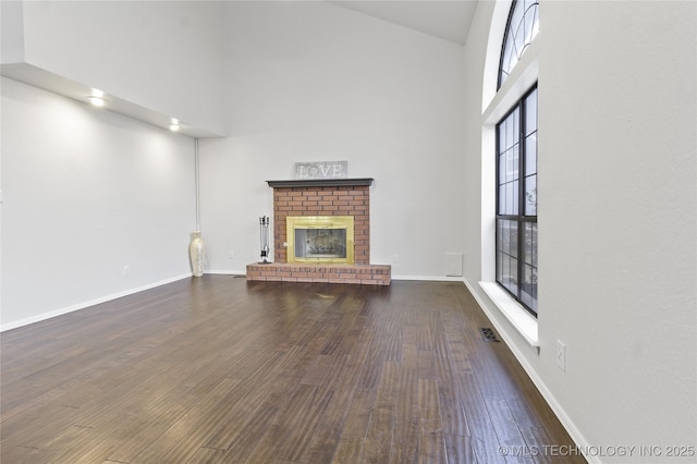 unfurnished living room featuring a towering ceiling, dark hardwood / wood-style flooring, and a brick fireplace