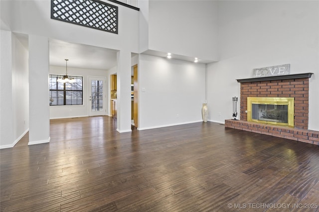 unfurnished living room with dark hardwood / wood-style floors, a towering ceiling, a fireplace, and a notable chandelier