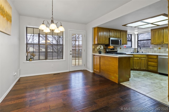 kitchen with sink, decorative light fixtures, appliances with stainless steel finishes, kitchen peninsula, and a healthy amount of sunlight