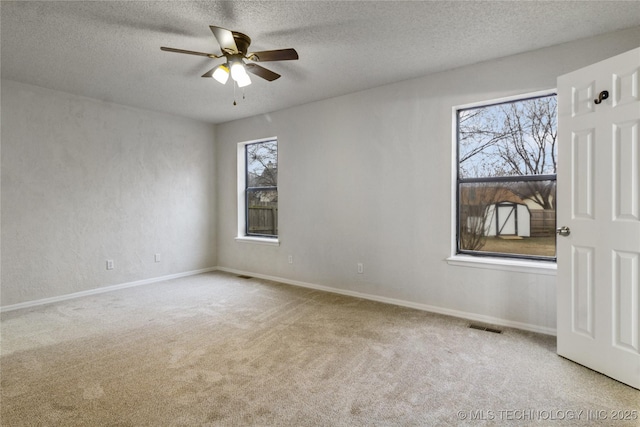 spare room with a textured ceiling, light colored carpet, and ceiling fan