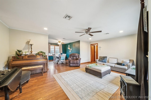 living room featuring ceiling fan, ornamental molding, and light wood-type flooring