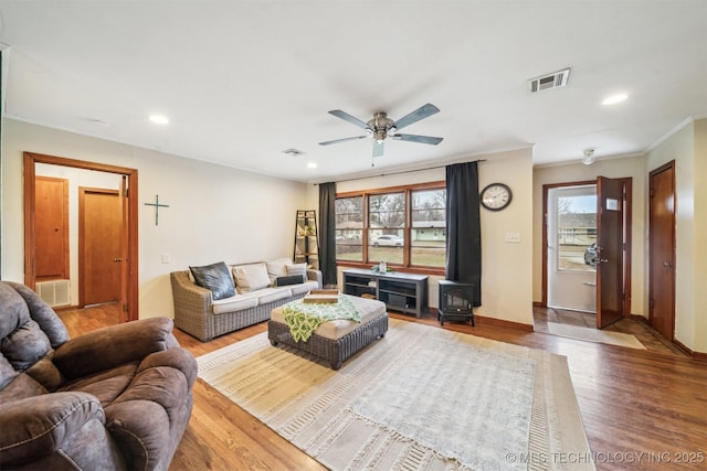 living room with wood-type flooring, a wood stove, a wealth of natural light, and ornamental molding