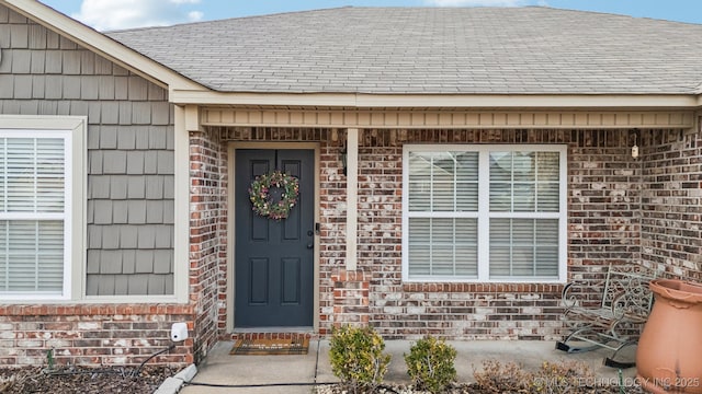 entrance to property featuring brick siding and roof with shingles