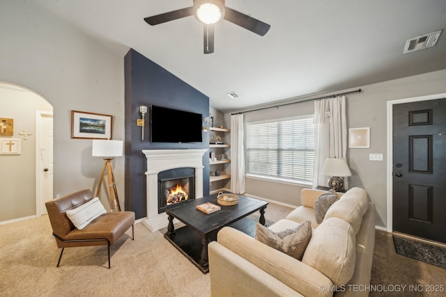 living area featuring a warm lit fireplace, visible vents, arched walkways, lofted ceiling, and carpet