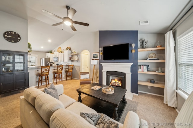 living room featuring lofted ceiling, a warm lit fireplace, visible vents, and a healthy amount of sunlight