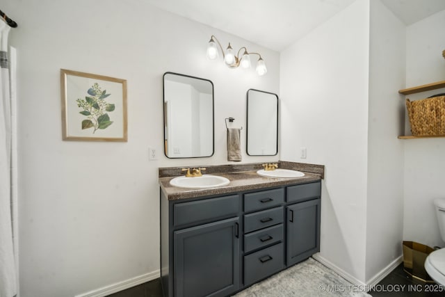 bathroom featuring baseboards, a sink, toilet, and double vanity