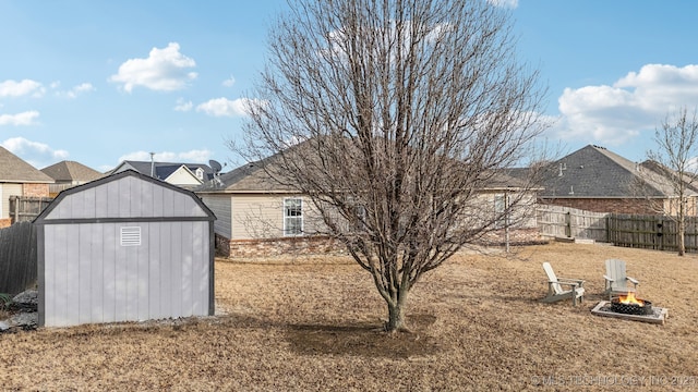 view of yard with an outdoor fire pit, fence, a storage unit, and an outdoor structure